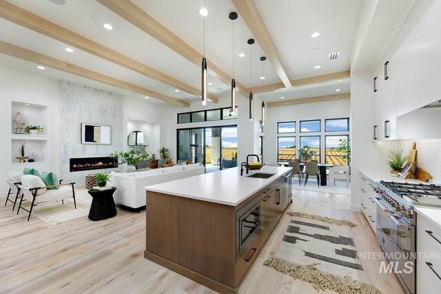 kitchen with appliances with stainless steel finishes, sink, pendant lighting, white cabinetry, and an island with sink