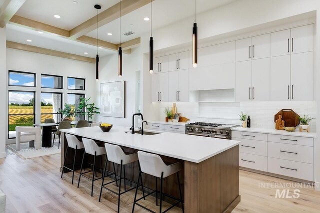 kitchen with beam ceiling, white cabinetry, sink, an island with sink, and high end stainless steel range