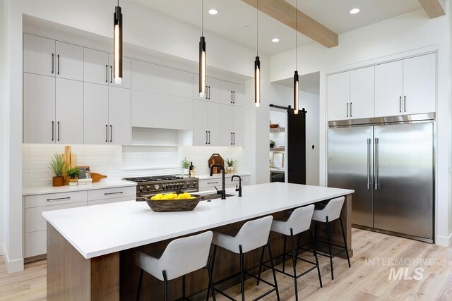 kitchen featuring beamed ceiling, high end appliances, an island with sink, and light hardwood / wood-style flooring