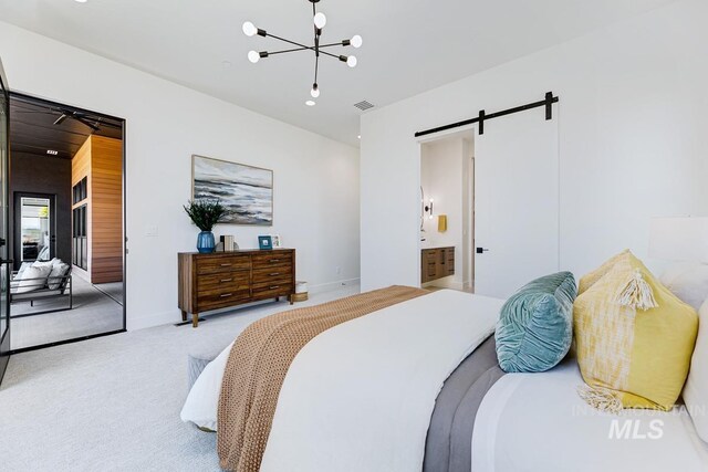 carpeted bedroom with ensuite bathroom, a barn door, and an inviting chandelier