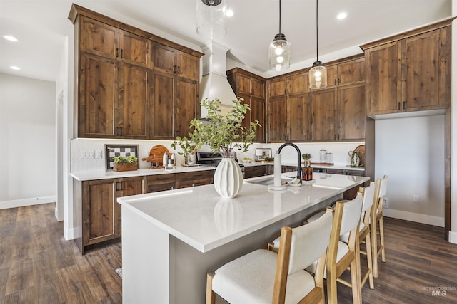 kitchen featuring dark hardwood / wood-style flooring, custom range hood, a kitchen island with sink, sink, and decorative light fixtures