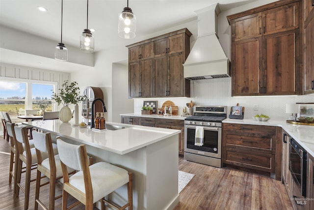 kitchen with premium range hood, gas range, sink, a center island with sink, and a breakfast bar area