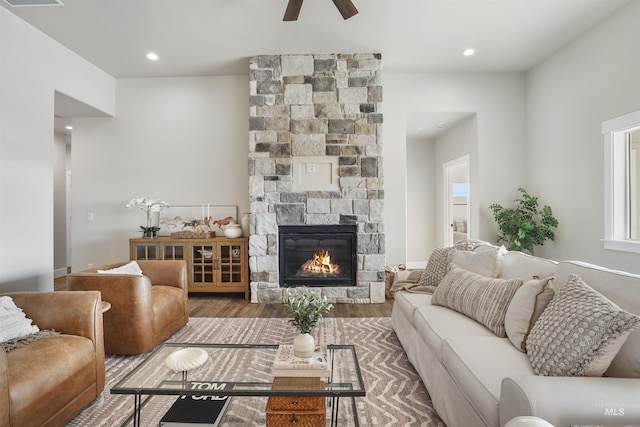 living room featuring hardwood / wood-style flooring, a stone fireplace, and ceiling fan