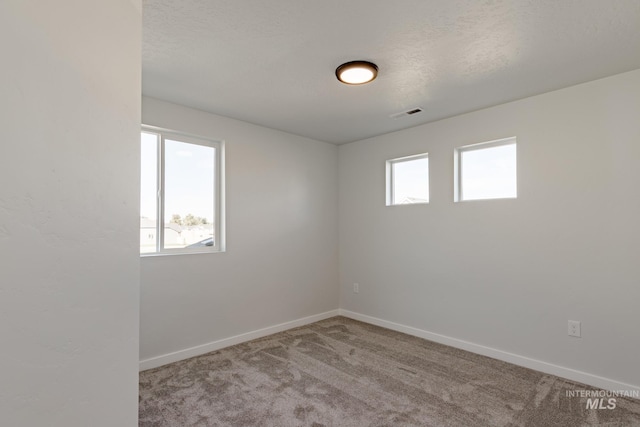 carpeted spare room with a wealth of natural light, visible vents, and baseboards