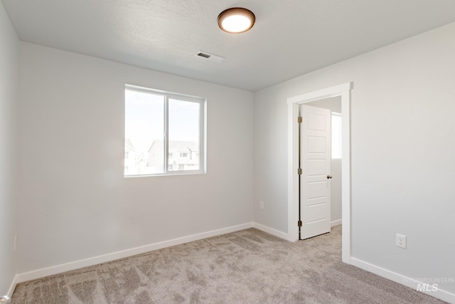 spare room with visible vents, baseboards, light colored carpet, and a textured ceiling