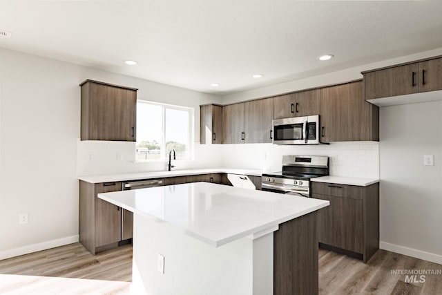 kitchen with baseboards, stainless steel appliances, light countertops, light wood-style floors, and tasteful backsplash