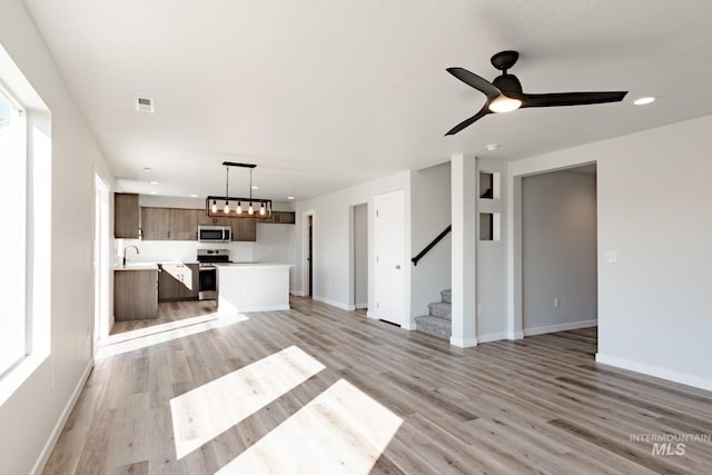 unfurnished living room with visible vents, baseboards, stairs, and light wood finished floors