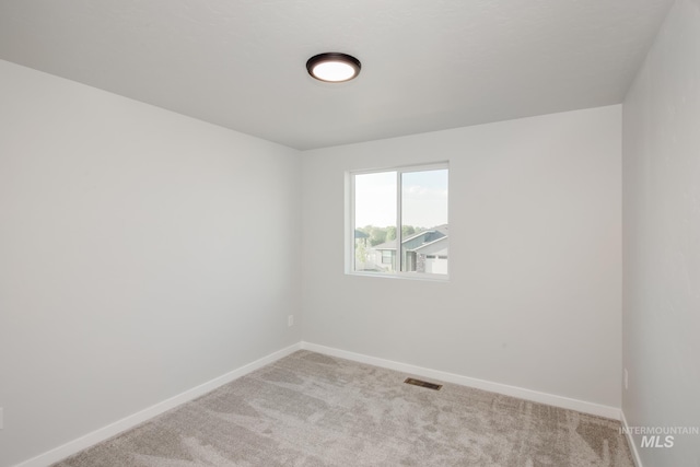 empty room featuring light colored carpet, visible vents, and baseboards