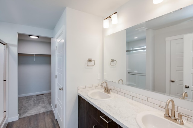 full bath with double vanity, a walk in closet, a sink, and wood finished floors