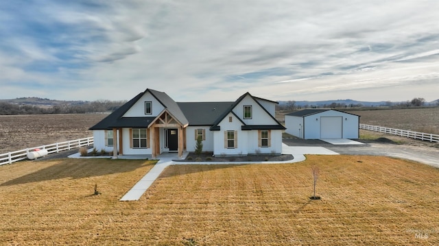 modern inspired farmhouse with a rural view, a detached garage, fence, a front yard, and an outbuilding