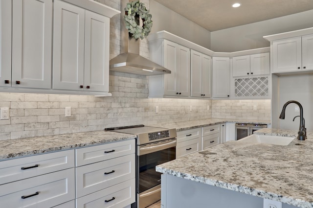 kitchen featuring stainless steel electric stove, white cabinetry, wall chimney range hood, and a sink