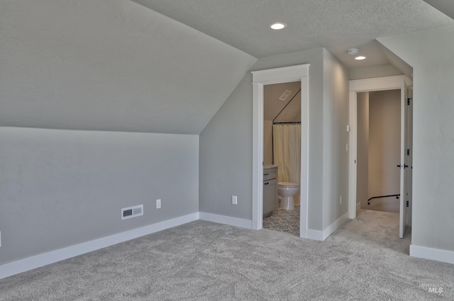 additional living space featuring visible vents, baseboards, vaulted ceiling, carpet floors, and a textured ceiling