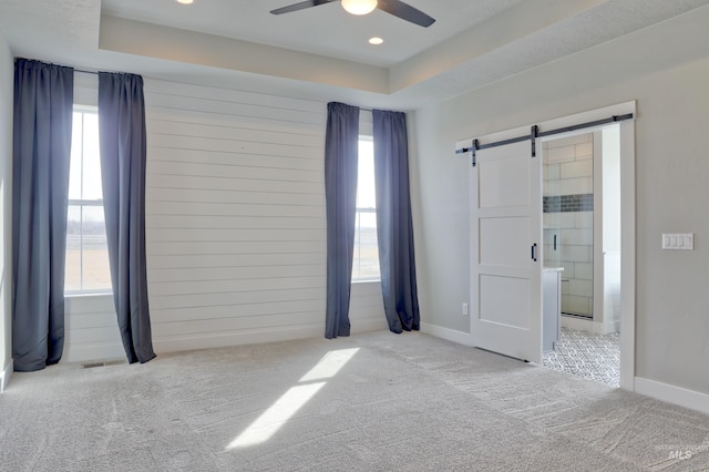 unfurnished bedroom featuring carpet flooring, a barn door, multiple windows, and a tray ceiling