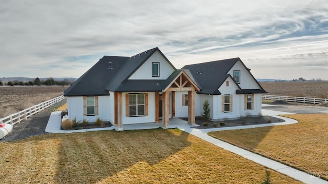 modern farmhouse featuring a rural view, a front yard, fence, and board and batten siding