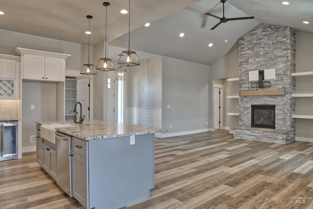 kitchen with a ceiling fan, open floor plan, wine cooler, light wood-style floors, and a stone fireplace