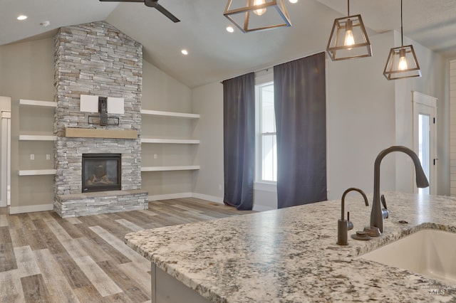 kitchen with ceiling fan, light stone countertops, a fireplace, wood finished floors, and a sink