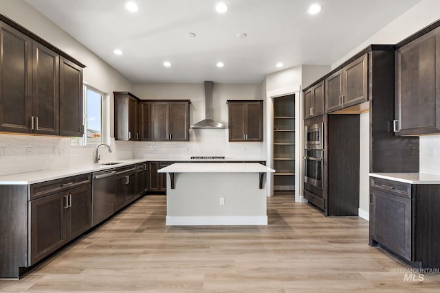 kitchen with wall chimney range hood, dark brown cabinets, light wood-style flooring, and appliances with stainless steel finishes