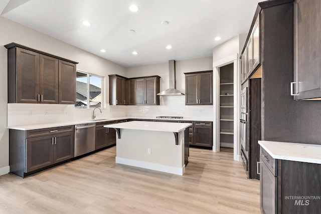 kitchen with a sink, stainless steel appliances, dark brown cabinetry, wall chimney range hood, and a center island