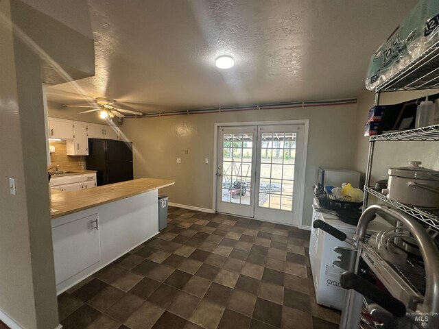 kitchen featuring white cabinetry, tasteful backsplash, ceiling fan, black refrigerator, and sink