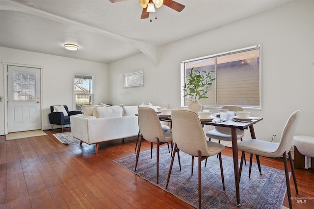 dining space featuring arched walkways, dark wood finished floors, a ceiling fan, and beamed ceiling