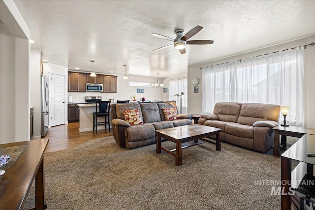 living room with a textured ceiling, dark wood-style flooring, and ceiling fan with notable chandelier