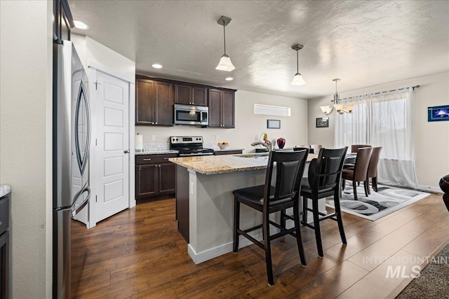 kitchen featuring a kitchen bar, a textured ceiling, dark wood-style floors, appliances with stainless steel finishes, and dark brown cabinets