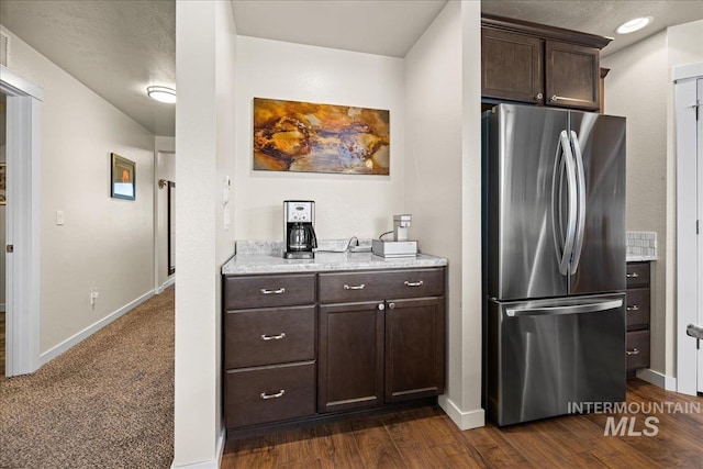 kitchen featuring dark wood-style flooring, dark brown cabinets, baseboards, and freestanding refrigerator