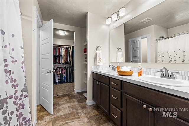 bathroom featuring a sink, visible vents, a spacious closet, and double vanity