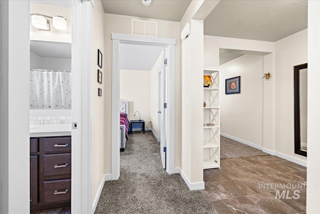 corridor with dark colored carpet, visible vents, and baseboards