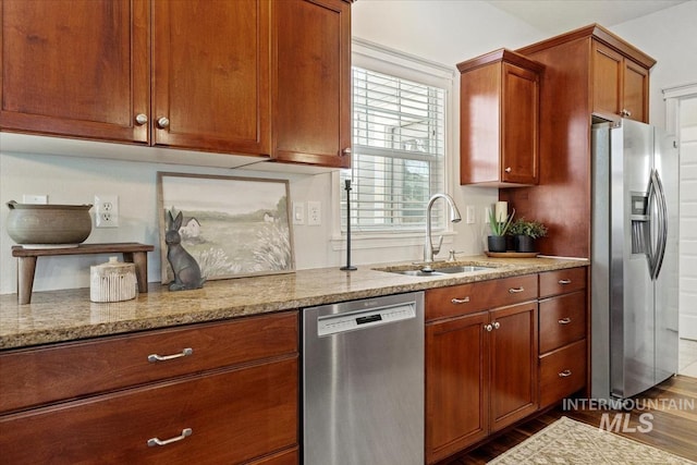 kitchen featuring brown cabinets, light stone countertops, stainless steel appliances, and a sink