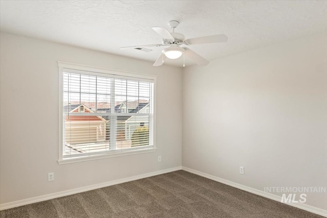 empty room featuring visible vents, a textured ceiling, dark colored carpet, baseboards, and ceiling fan