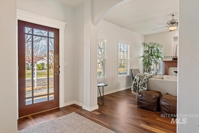 entryway featuring dark wood-style floors, arched walkways, a fireplace, baseboards, and ceiling fan