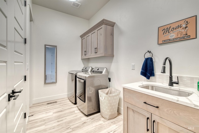laundry area featuring visible vents, washing machine and dryer, a sink, cabinet space, and light wood finished floors