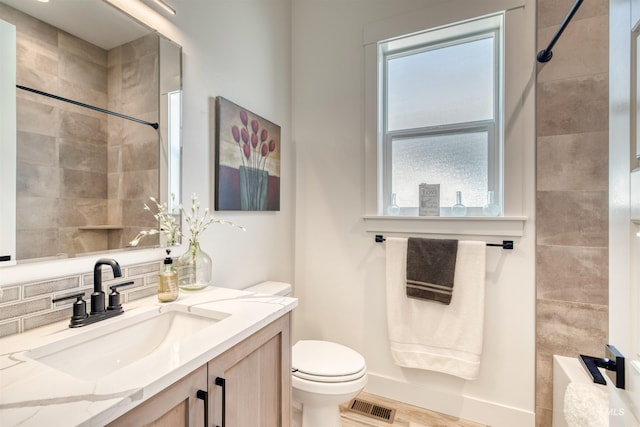 bathroom with toilet, visible vents, a tile shower, and vanity