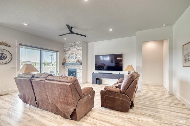 living area featuring a stone fireplace, light wood-style flooring, a ceiling fan, baseboards, and recessed lighting