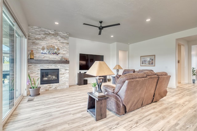 living area with ceiling fan, a stone fireplace, wood finished floors, baseboards, and recessed lighting