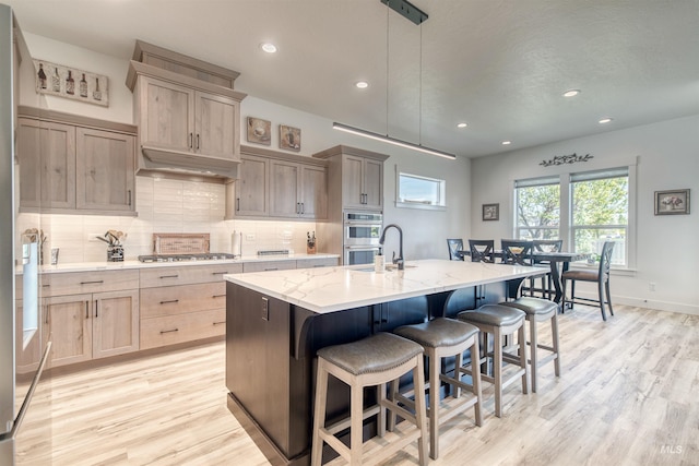 kitchen with appliances with stainless steel finishes, a breakfast bar, a kitchen island with sink, light wood-style flooring, and decorative backsplash