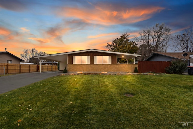 mid-century inspired home featuring an attached carport, brick siding, fence, driveway, and a front lawn