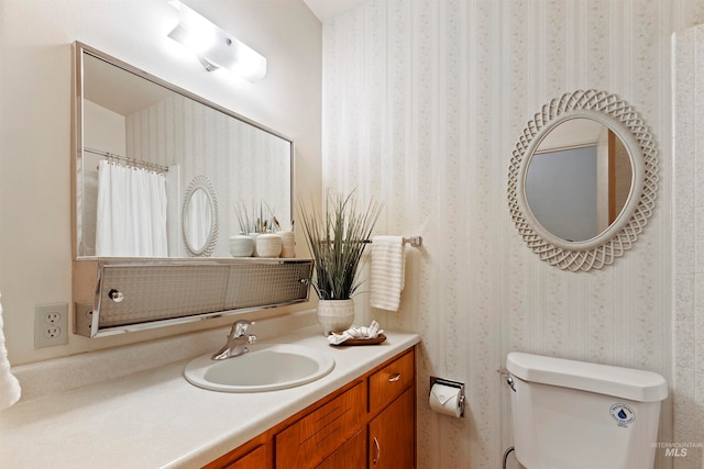 bathroom with toilet, wallpapered walls, and vanity