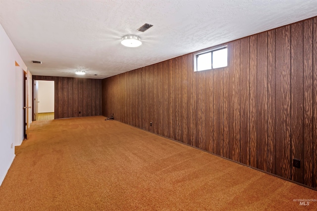 basement featuring visible vents, light colored carpet, wood walls, and a textured ceiling