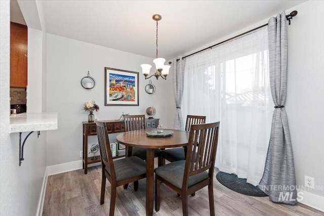 dining area with baseboards, a notable chandelier, and light wood finished floors