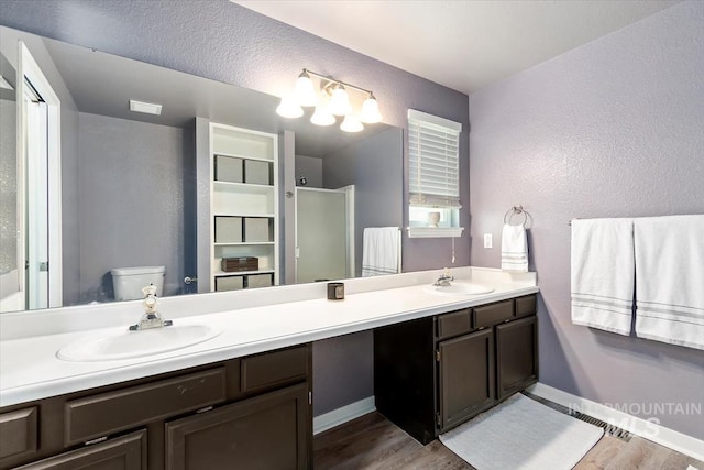 bathroom with a sink, double vanity, toilet, and wood finished floors