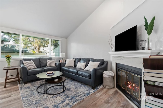living room featuring a glass covered fireplace, wood finished floors, and vaulted ceiling