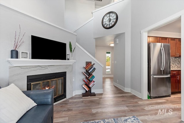 living room featuring a towering ceiling, a fireplace, light wood-style floors, baseboards, and stairway