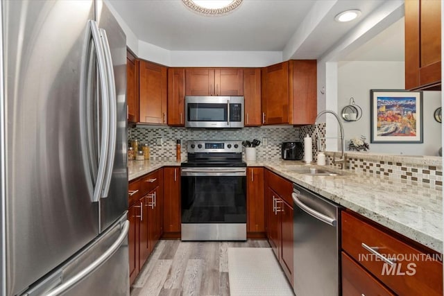 kitchen with light stone counters, a sink, stainless steel appliances, decorative backsplash, and light wood-type flooring