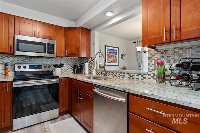 kitchen featuring a sink, decorative backsplash, appliances with stainless steel finishes, and light stone countertops