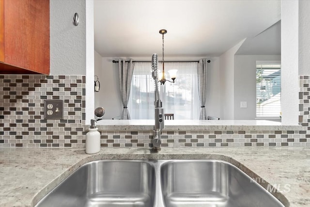 room details featuring a sink, backsplash, brown cabinets, and light stone countertops