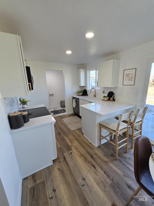 kitchen with dark wood-type flooring, white cabinetry, decorative backsplash, kitchen peninsula, and stainless steel dishwasher