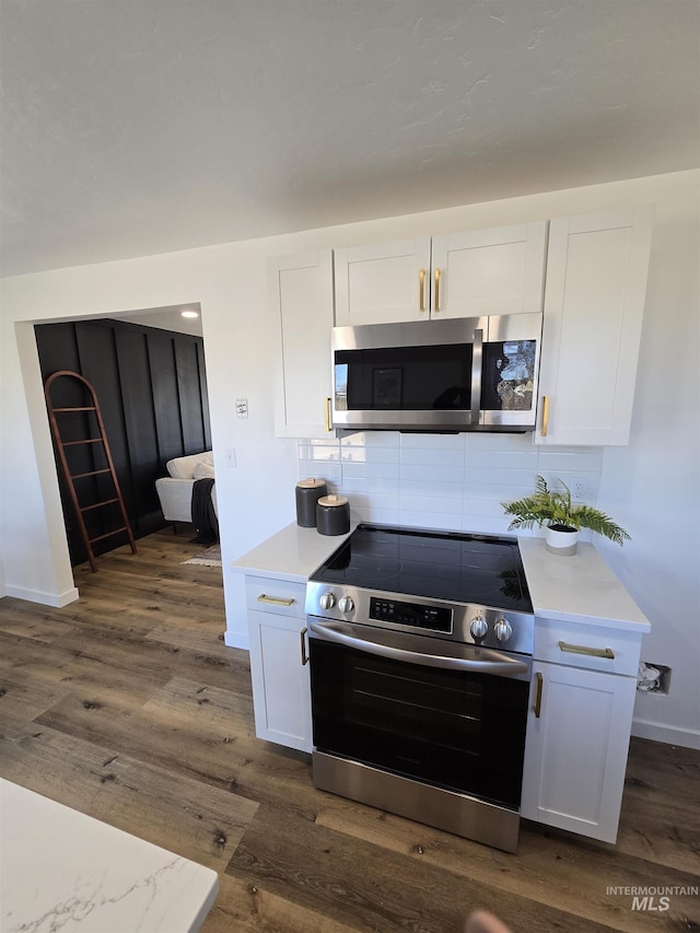 kitchen with white cabinets, backsplash, appliances with stainless steel finishes, and dark hardwood / wood-style flooring