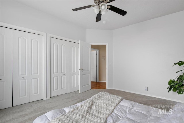 bedroom featuring ceiling fan, light carpet, and two closets